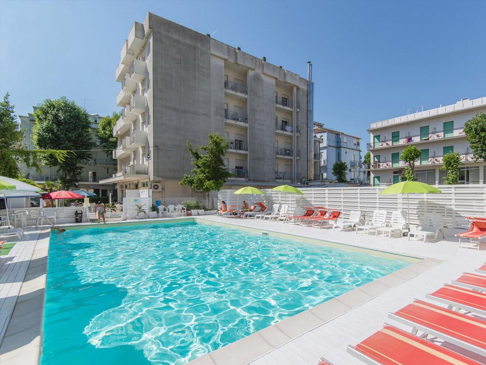 Piscina soleggiata, ombrelloni colorati, sedie a sdraio, atmosfera estiva e rilassante.